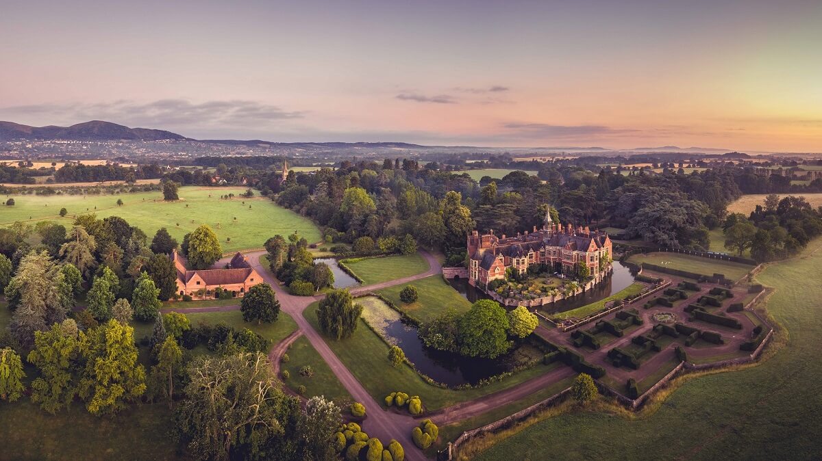 Aerial view of Madresfield Court with moat and gardens and outline of Malvern Hills in background