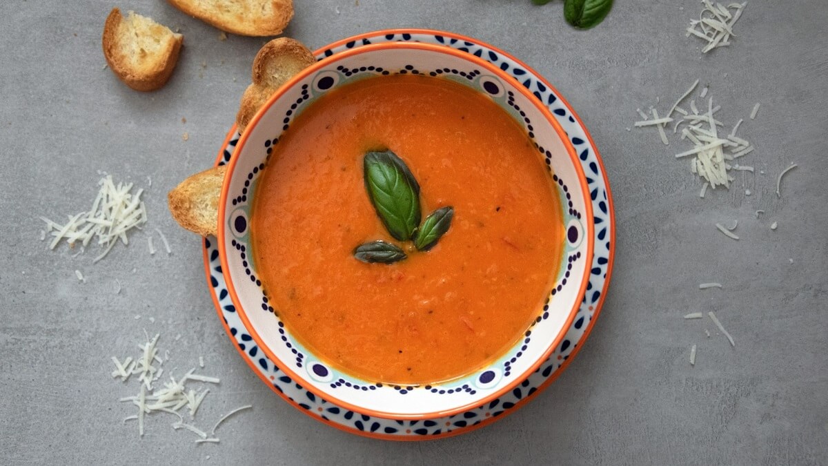 A bowl of soup garnished with basil, placed on a grey surface